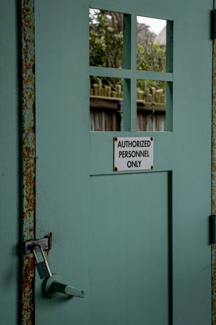 A close-up view of a black and white 'No Trespassing' sign attached to a dark door, with the sign featuring a bold black background, white uppercase text, and a blank white space underneath for additi